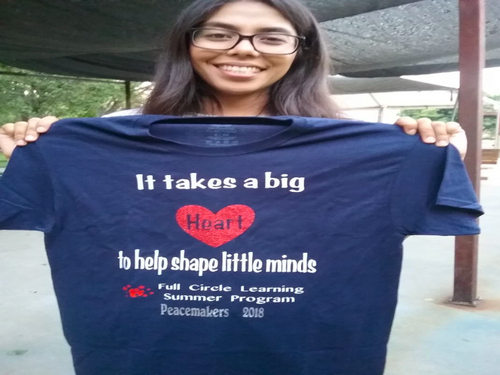 A woman holds up a t-shirt that says 'It takes a big heart to to help shape little minds.'