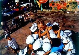 A man is crowded by several children in celebration of painting neighborhood walls