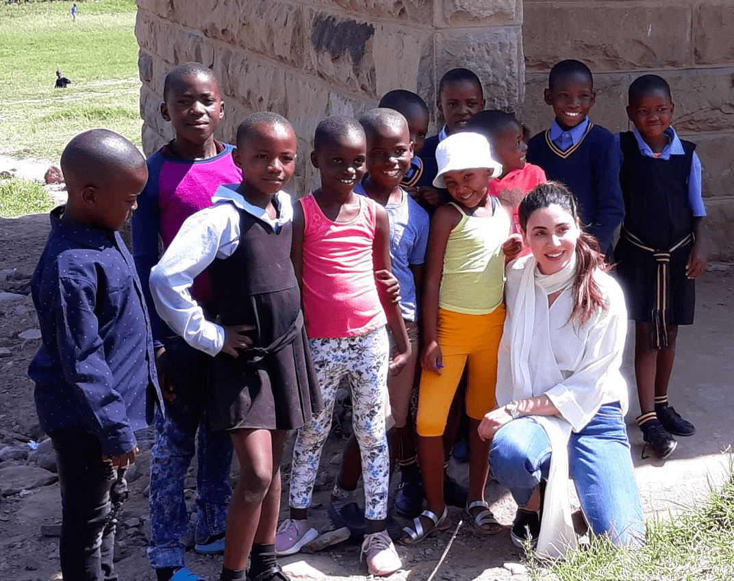 Sana kneels in front of children grouped together for.