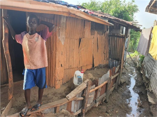 A boy stands outside his home.