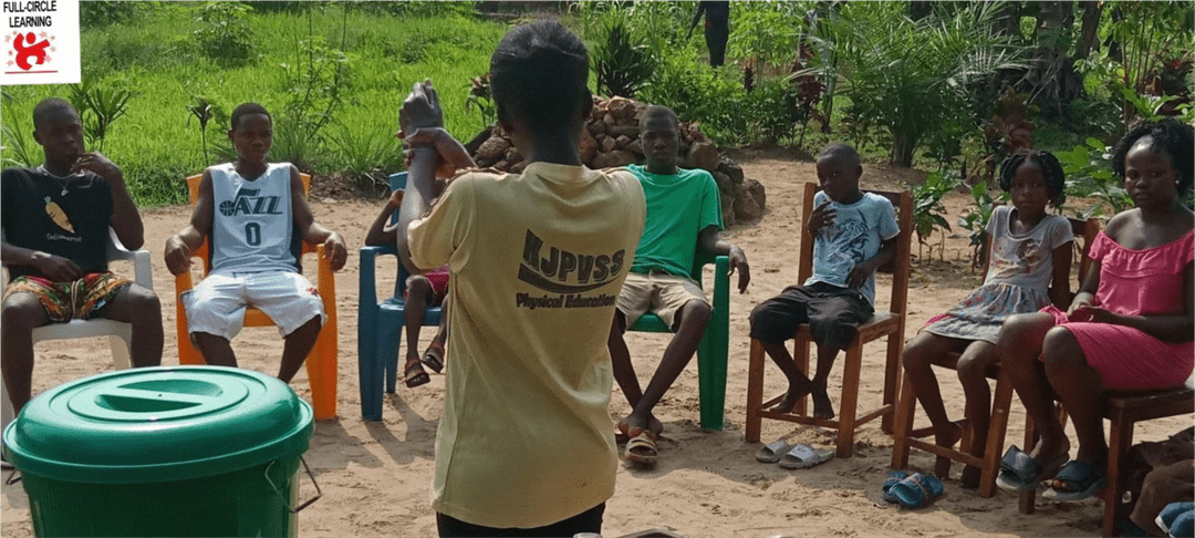 A student is sharing knowledge with the rest of the className seated outside.